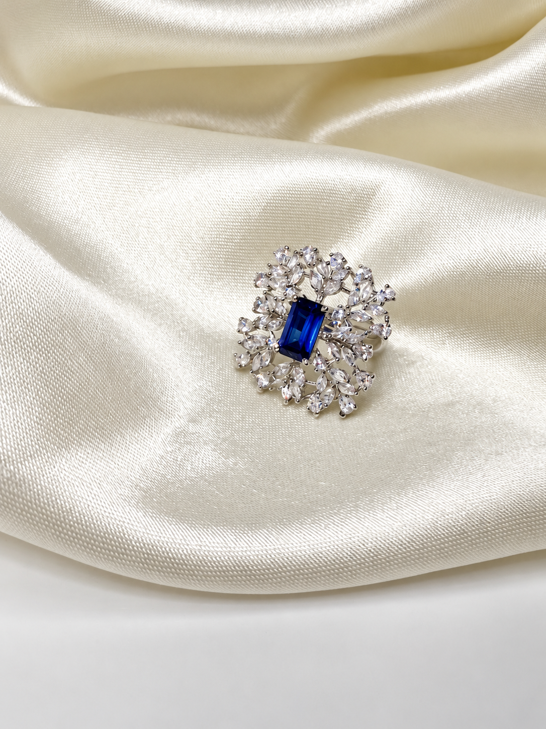 Blue-centred Sapphire Snowflake Cocktail Ring styled on a hand against ivory satin