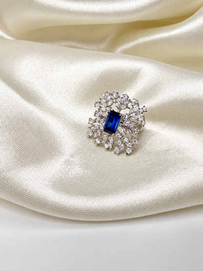 Blue-centred Sapphire Snowflake Cocktail Ring styled on a hand against ivory satin