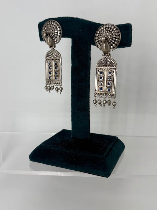 A pair of silver-toned Indian jhumka earrings with blue stone accents, displayed on a black velvet T-stand against a white background.