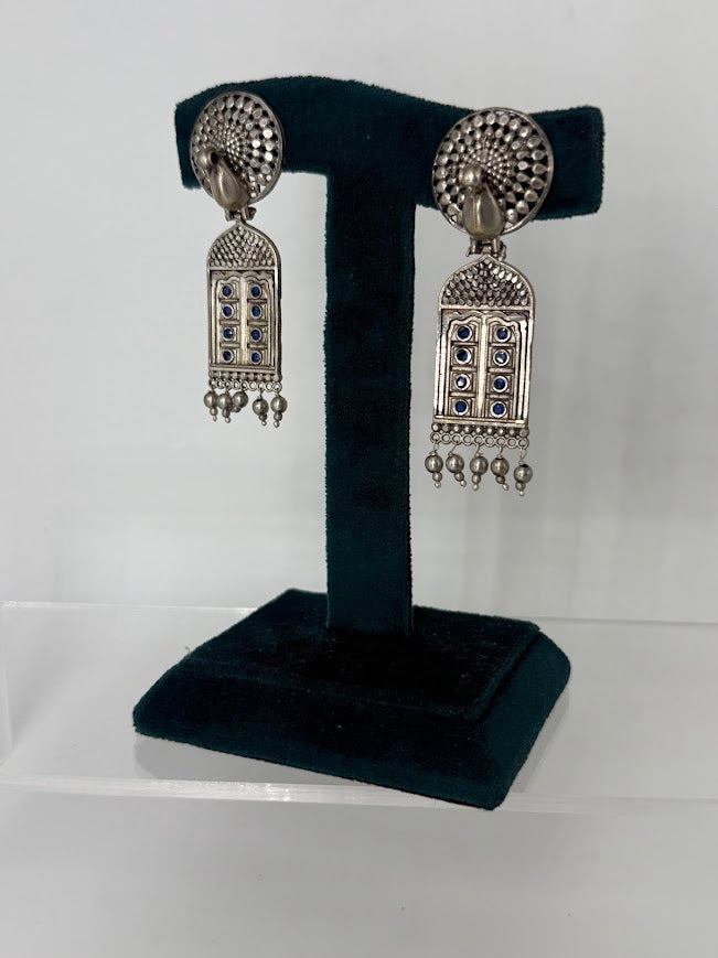 A pair of silver-toned Indian jhumka earrings with blue stone accents, displayed on a black velvet T-stand against a white background.